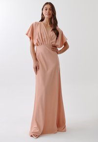 Maxi dress in light peach, made of smooth fabric. Features a deep V-neck, gathered waist, and short, wide sleeves. Simple, elegant design.