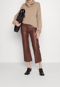 Beige coltrui, bruine nepleer cropped pants en zwarte blokhak mules. De outfit wordt aangevuld met een gequilt zwarte handtas.