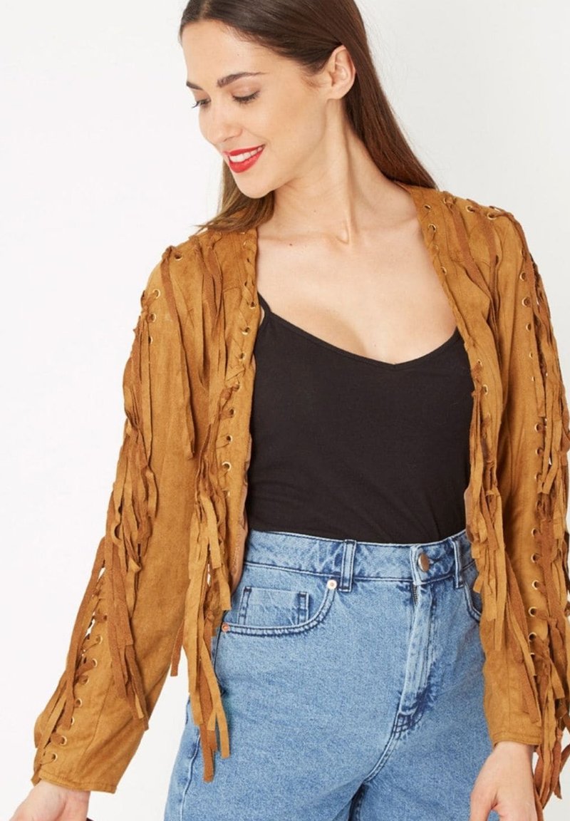 Chaqueta de ante marrón con detalles de flecos, acentos de cordones y mangas largas, combinada con una blusa negra y vaqueros de cintura alta de color azul claro.