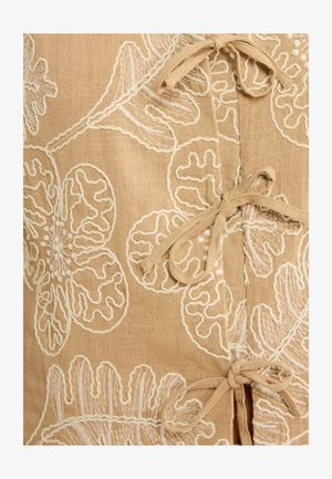 Pruun kangas valge lillemustriga tikandiga ja kolm seotud lipsu esiosas oleva ava ääres.