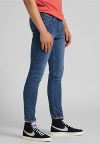 Jeans skinnies de mezclilla azul con una textura suave y un ajuste ceñido, combinados con zapatillas altas negras con detalles grises y cordones blancos.