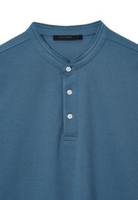 Maglietta henley blu a maniche corte realizzata in tessuto testurizzato, con scollatura rotonda, tre bottoni bianchi e un'etichetta interna.