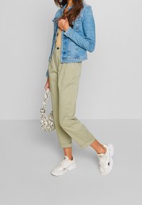 Light blue denim jacket, beige ribbed top, olive green trousers, white sneakers, and a white snake-print handbag.
