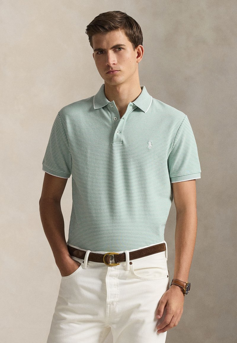 Striped mint green polo shirt with a collar, three-button placket, and a small logo. Worn with white trousers and a brown belt.
