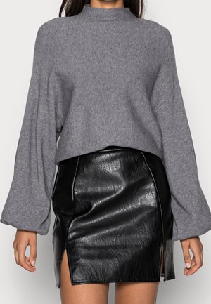 Szary dziany sweter z szerokimi rękawami, zestawiony z czarną skórzaną mini spódnicą z bocznym rozcięciem i błyszczącą fakturą.