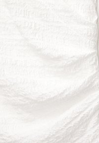 Gros plan d'un tissu blanc avec une texture froncée et des plis doux, montrant des motifs détaillés de rides.