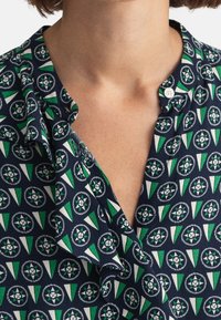 Camicia navy con un motivo geometrico caratterizzato da accenti verdi e bianchi. Tessuto morbido, colletto con bottoni e design dalla vestibilità rilassata.