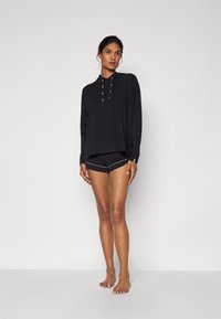 Felpa nera a maniche lunghe con tasca a marsupio e coulisse, abbinata a pantaloni corti neri con cucitura a contrasto in vita.
