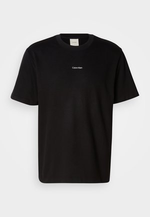 Mustapaita, jossa on lyhyet hihat, pyöreä pääntie ja valkoinen "Calvin Klein" -logo keskellä rintaa. Sujuva rakenne, klassinen istuvuus.
