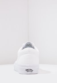 Baskets blanches Vans vues de l'arrière, montrant les détails cousus du talon et le logo "Vans Off The Wall" sur le talon de la semelle.