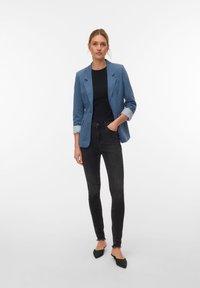 Lichtblauwe blazer met opgerolde manchetten, zwarte top en nauwsluitende zwarte jeans. De blazer heeft een kentkraag en twee knopen.