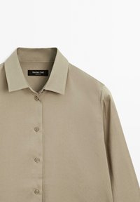 Lichtbeige overhemd met knopen en een puntige kraag, gemaakt van gladde stof. Heeft een centrale knopenlijst met vijf knopen. Merklabel zichtbaar.