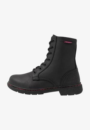 Bottine noire à lacets en cuir synthétique, avec des surpiqûres rouges, une semelle plate et un logo embossé sur le côté extérieur.