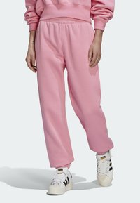 Rosa sweatpants i mjukt tyg, med elastisk midja och smalnade anklar, kombinerat med vita sneakers med svarta ränder.