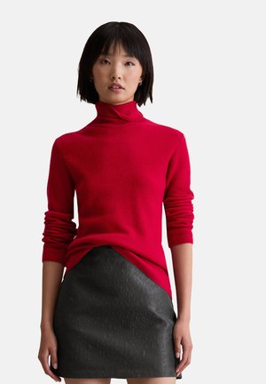 Red ribbed turtleneck sweater with long sleeves, paired with a black textured mini skirt featuring a smooth finish and subtle pattern.