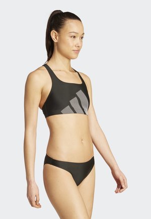 Black sports bra with a textured gray geometric pattern and adjustable straps, paired with matching low-cut bikini bottoms. Smooth, stretchy fabric.