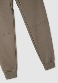 Brązowe spodnie dresowe wykonane z miękkiego materiału, z nogawkami zwężanymi ku dołowi, ściągaczami na końcach i wzorem przeszyć panelowych. Brak widocznych kieszeni.