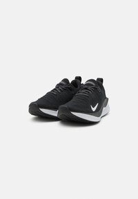 Chaussures de sport noires avec un dessus en tissu texturé, des lacets gris, des accents blancs et une semelle en caoutchouc noire avec un motif de crampons.