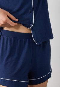 Marinblå bomullsoverall med vit kantning, som har en löst sittande knäppskjorta och shorts med elastisk midja. Den mjuka texturen är synlig.