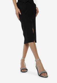 Falda negra ajustada con una abertura, combinada con sandalias plateadas de tiras con acentos de strass y suelas negras. Textura suave y diseño elegante.