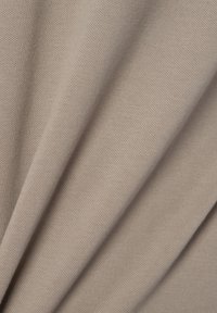 Beiger, strukturierter Stoff mit einem Strickmuster, das sanfte Falten und eine glatte Oberfläche zeigt. Das Material wirkt langlebig und flexibel.