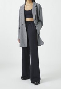 Blazer a cuadros en blanco y negro sobre un top corto negro, combinado con pantalones negros holgados. Tejido suave, ajuste a medida y silueta relajada.