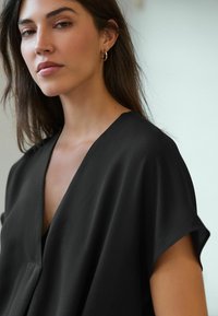 Schwarze V-Ausschnitt-Bluse mit kurzen Ärmeln, aus glattem Stoff, mit lockerer Passform und subtilen Drapierungsdetails.