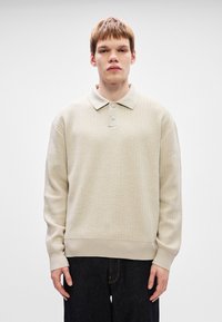 Pulover polo tricotat bej, cu un model texturat, nasturi la guler și tiv ribbat. Purtați cu pantaloni din denim închisi.