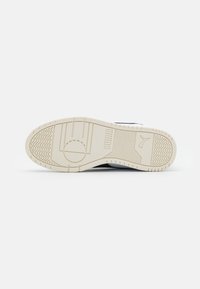 Witte sneakerzool met een gestructureerde, crème-kleurige rubberen zool, met een PUMA-logo en verschillende loopprofielen voor grip.