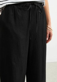 Zwarte wijde broek gemaakt van een textuurstof, met een trekkoord in de taille en een losse pasvorm.