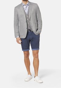 Grå blazer i ullblandning med två knappar och fickor; kombinerad med en blå blommig skjorta, navy-rutiga shorts och vita sneakers.