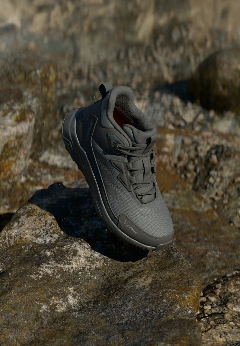 Gray athletic shoe with a textured surface, high ankle support, and a cushioned interior, displayed against a rocky background.