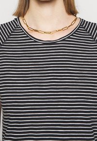 Svart- och vitrandig croppad topp med rundad halsringning. Har en mjuk textur och ett gyllene kedjearmband med avlånga länkar som accent.