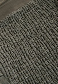 Gros plan sur un tissu vert olive avec des coutures froncées et serrées créant une surface texturée et élastique.