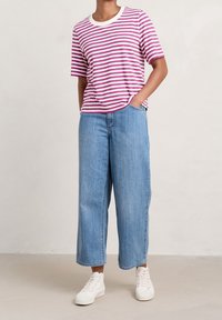 Striped purple and white t-shirt with a crew neck, paired with light blue wide-leg jeans and white sneakers, on a neutral background.