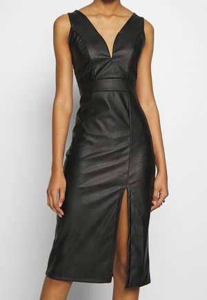 Robe midi noire sans manches en similicuir avec décolleté plongeant en V, taille cintrée et fente avant, portée par une personne debout devant un fond uni.