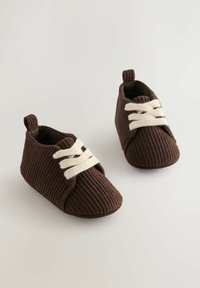 Brune fløjlsbaby sko med hvide snørebånd, med et lavt snit og små hæl detaljer. Blød tekstur og fleksibel konstruktion.