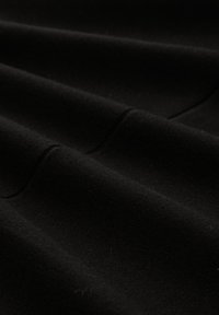 Acercamiento de una suave tela negra con sutiles pliegues y detalles visibles de costura.