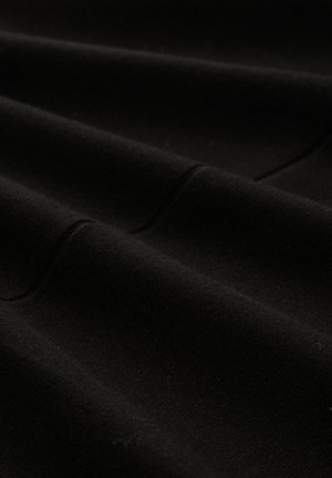 Tuvumā redzams mīksts melns audums ar smalkiem krokām un redzamām šuvju detaļām.