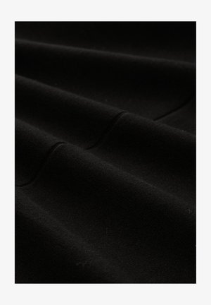 Nahaufnahme von weichem, schwarzem Stoff mit dezenten Falten und sichtbaren Nahtdetails.