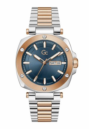 Runde Uhr mit marineblauem Zifferblatt, goldenen und silbernen Markierungen, Tages- und Datumsanzeige, goldener Lünette und zweifarbigem Metallarmband.