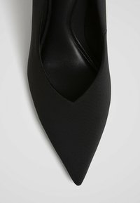 Svart spetsig tå stiletto-sko med en elegant, satinliknande finish och en slät textur, med en djup V-skärning runt fotryggen.