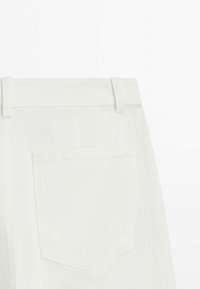 Back view of white denim skirt with belt loops and a single patch pocket on the right side.