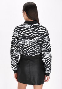 Blusa con patrón de cebra en blanco y negro, de manga larga, con puños acanalados y un diseño corto, combinada con una falda ajustada de piel sintética negra.