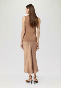 Beżowy, dzianinowy top bez rękawów zestawiony z długą, jedwabistą spódnicą w odcieniu beżu. Posiada dopasowany krój oraz brązowe, wysokie szpilki z sznurowaniem.