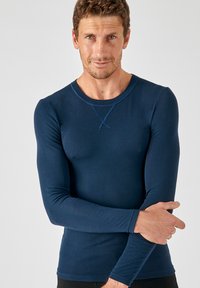 La camicia fitted a maniche lunghe di colore blu navy presenta un collo rotondo con un accento a punto croce e un tessuto liscio e elasticizzato.