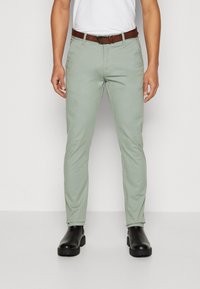 Lichtgroene chinos met een slim fit, een soepele textuur en een bruine leren riem. Draagt bij met zwarte enkellaarsjes.