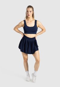 Navy blauwe sportbeha en geplooide rok set. De beha heeft een brede band, en de rok heeft een uitlopende silhouet met een gladde textuur.