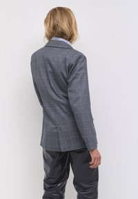 Niebieska marynarka w kratę, wykonana z teksturowanej tkaniny, z klapami. Posiada paskowany wewnętrzny kołnierz, dopasowany krój oraz dwa boczne rozcięcia.