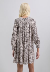 Vestido de estampado floral con mangas largas, escote fruncido, diseño en capas y fondo beige con manchas de leopardo en marrón y negro.